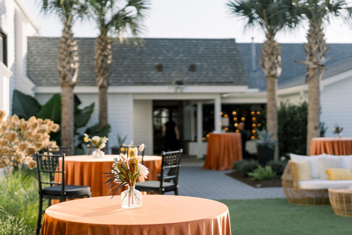 Orange linens and pink and yellow fall floral centerpieces for cocktail hour at Kindred Wedding and Events in Carolina Beach, NC. Planned by Brittanie Raquel Events. 