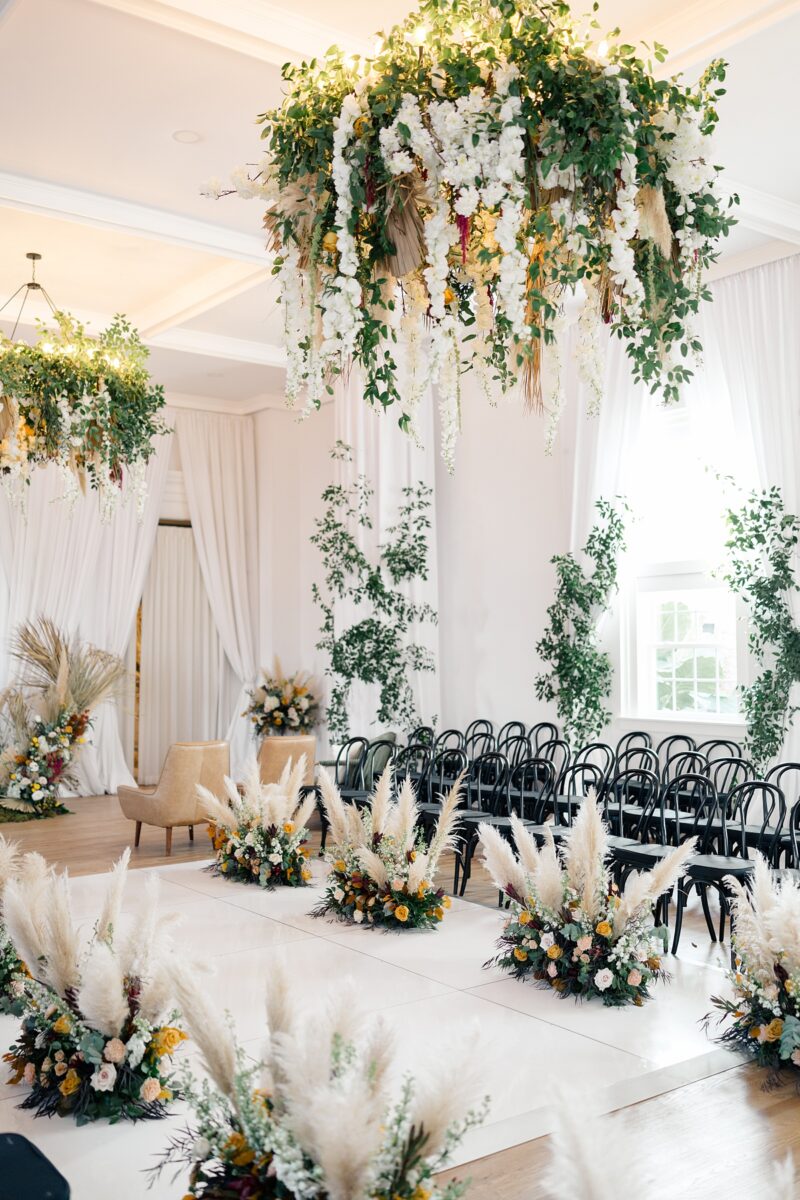 Fall orange, yellow, wine, white, and boho floral arrangement and hanging installation at Kindred Wedding and Event venue. Wedding planned by Brittanie Raquel Events. 