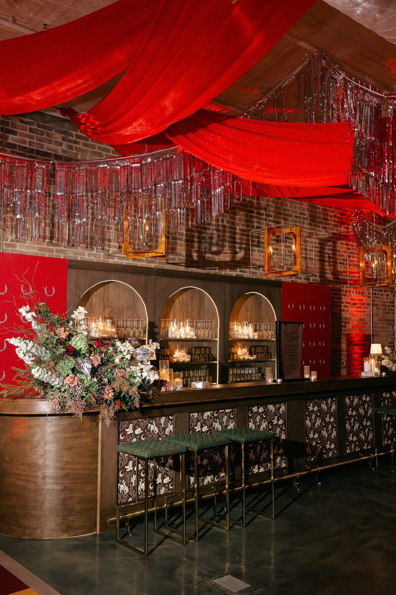Deep red and tinsel draping over a western saloon themed cocktail bar. Hosted at The Elia in Downtown Wilmington, NC by Brittanie Raquel Events. 