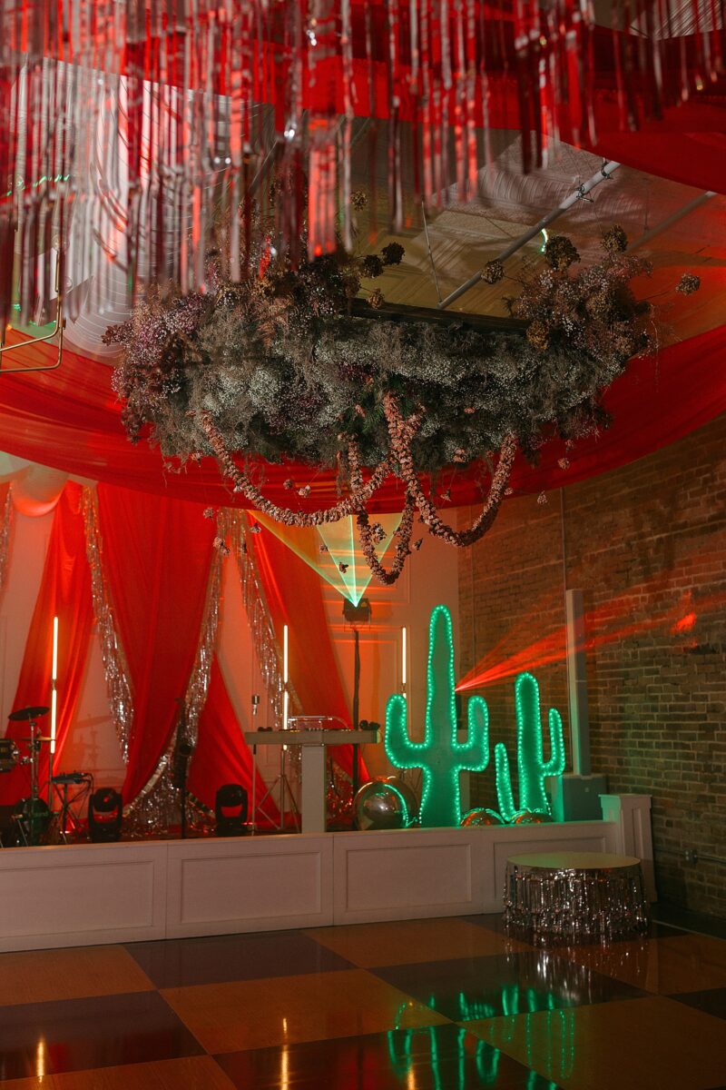 A hanging floral installation with dried carnations and red and tinsel draping. An event by Brittanie Raquel Events in Wilmington, NC.