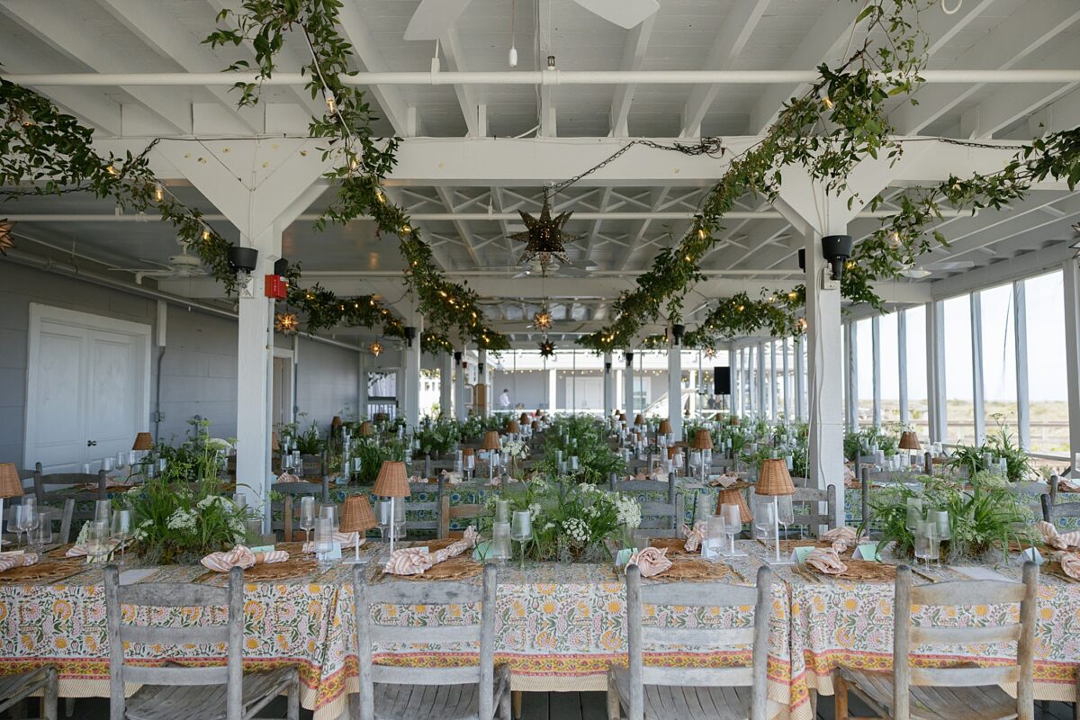 Wedding reception dinner room on screened-in porch on Wrightsville beach with patterned table clothes and a lot of green floral arrangements 
