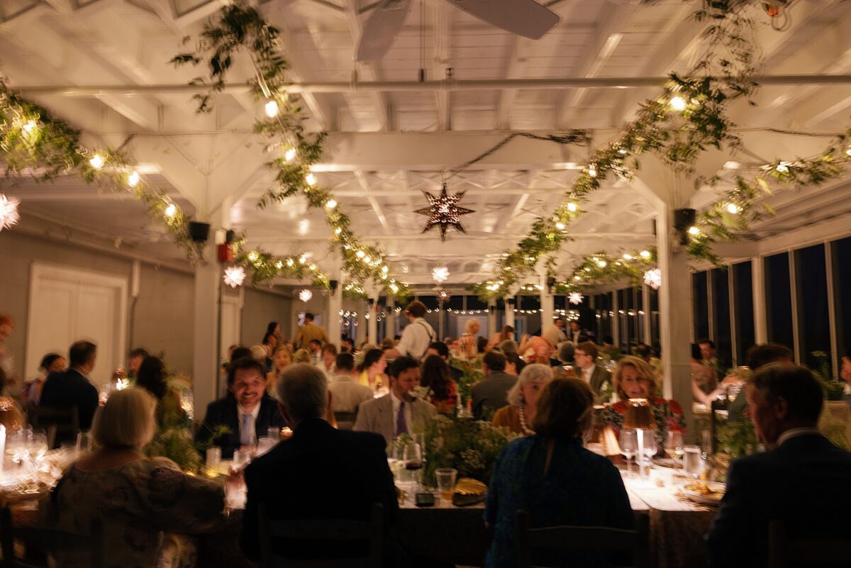 Wedding guests enjoying a dinner on a screened-in porch with romantic glow of lamps