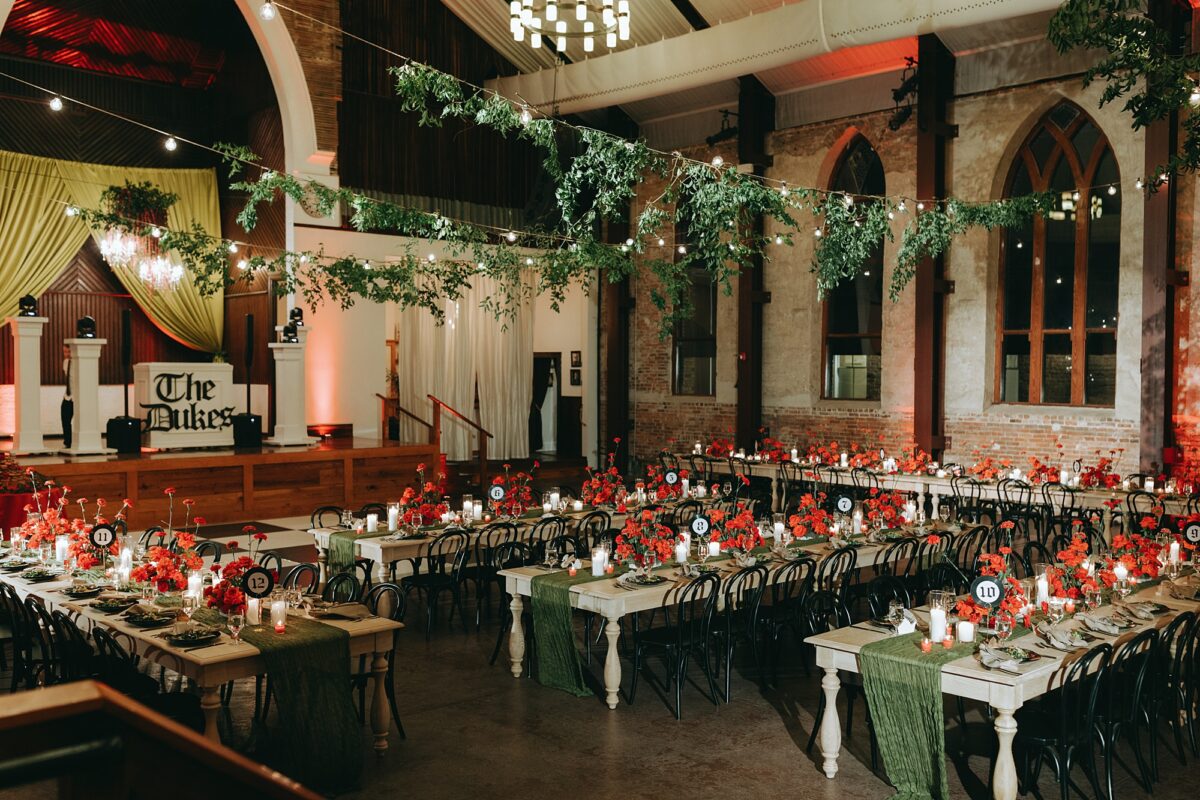 Wide shot of wedding reception table decor with dramatic red roses and crystal chandeliers for gothic rock and roll wedding at Brooklyn Arts Center
