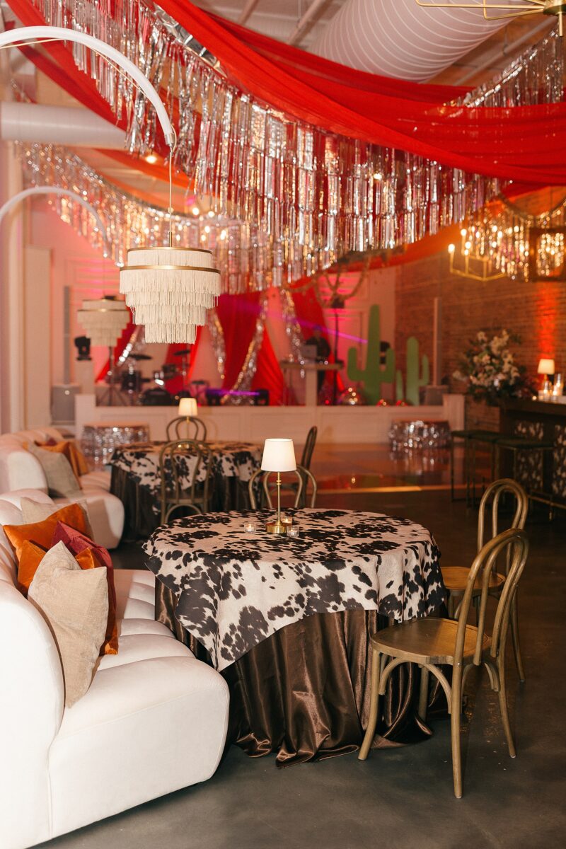 Western-themed table decor with cow print fabric and wooden chairs for Disco Rodeo party event at The Elia