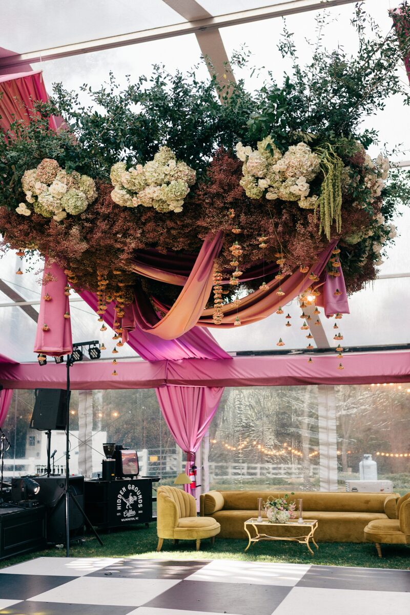Pink and green hanging floral arrangement from Mother of Wild over black and white checkered dance floor in tent wedding at Sycamore Bend